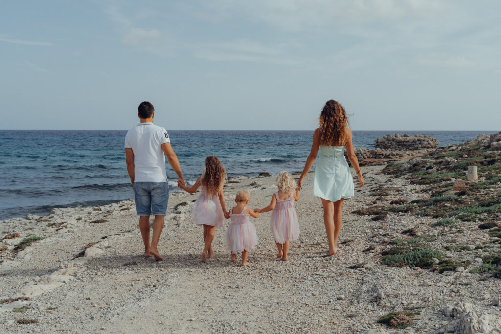 Familie mit 2 Kindern läuft an der Cala Mesquida an den Felsen entlang mit Blick aufs Meer.
