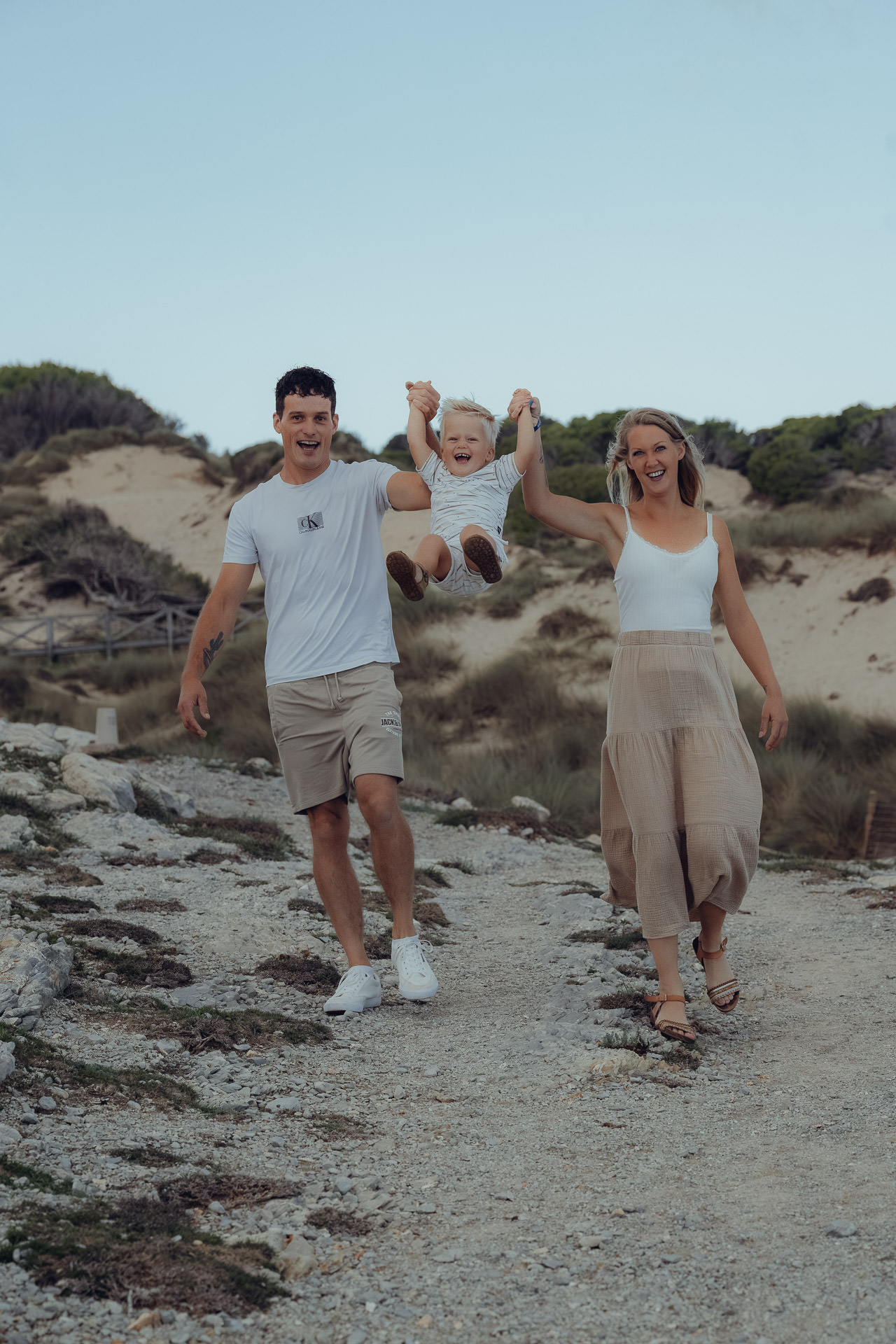 Familienfotoshooting Cala Mesquida – Eltern heben ihr Kind gemeinsam in die Luft, Lebensfreude am Strand von Mallorca.