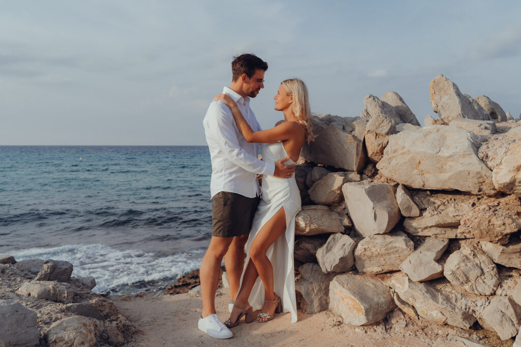 Verliebtes Paar steht auf den Felsen an der Cala Mesquida und schaut sich tief in die Augen.