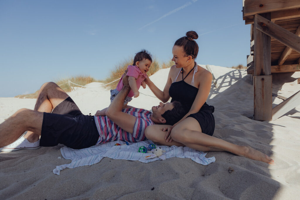 Eltern liegen mit ihrem Baby im Schatten der Holzbrücke an der Cala Mesquida