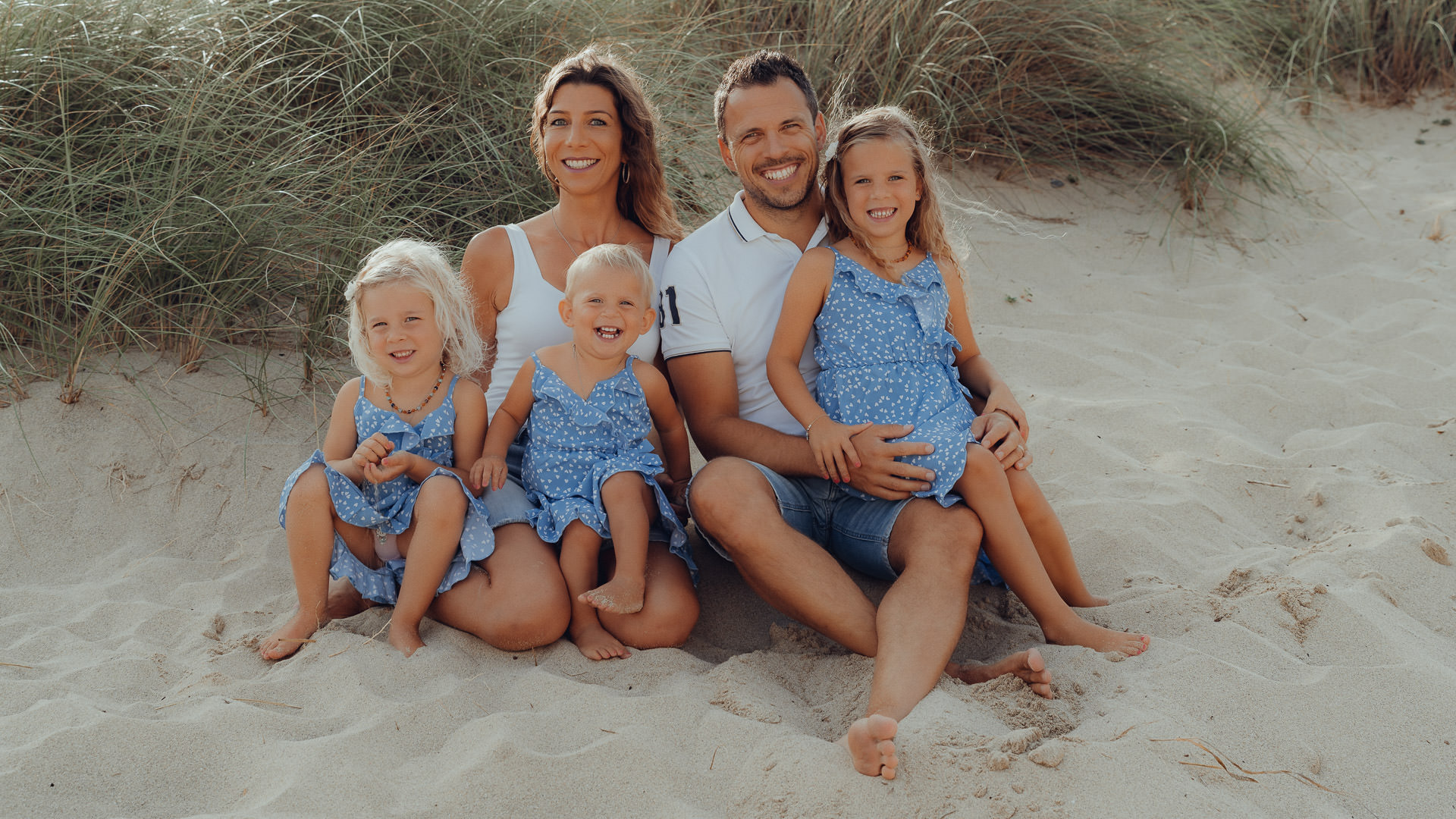 Cala Mesquida Fotoshooting 5 Köpfige Familie sitzt iim Sand der Cala Mesquida und schaut in die Kamera