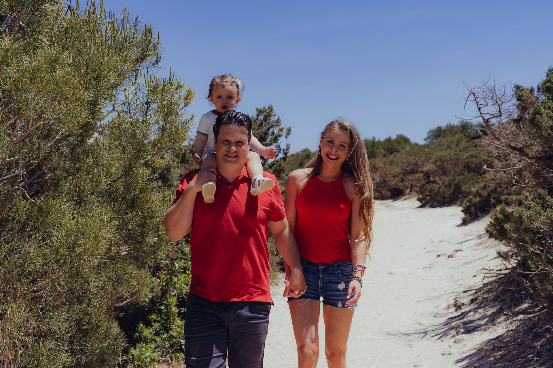 Familie mit kleinem Kind spaziert auf einem Sandweg durch die Dünen von Cala Millor.