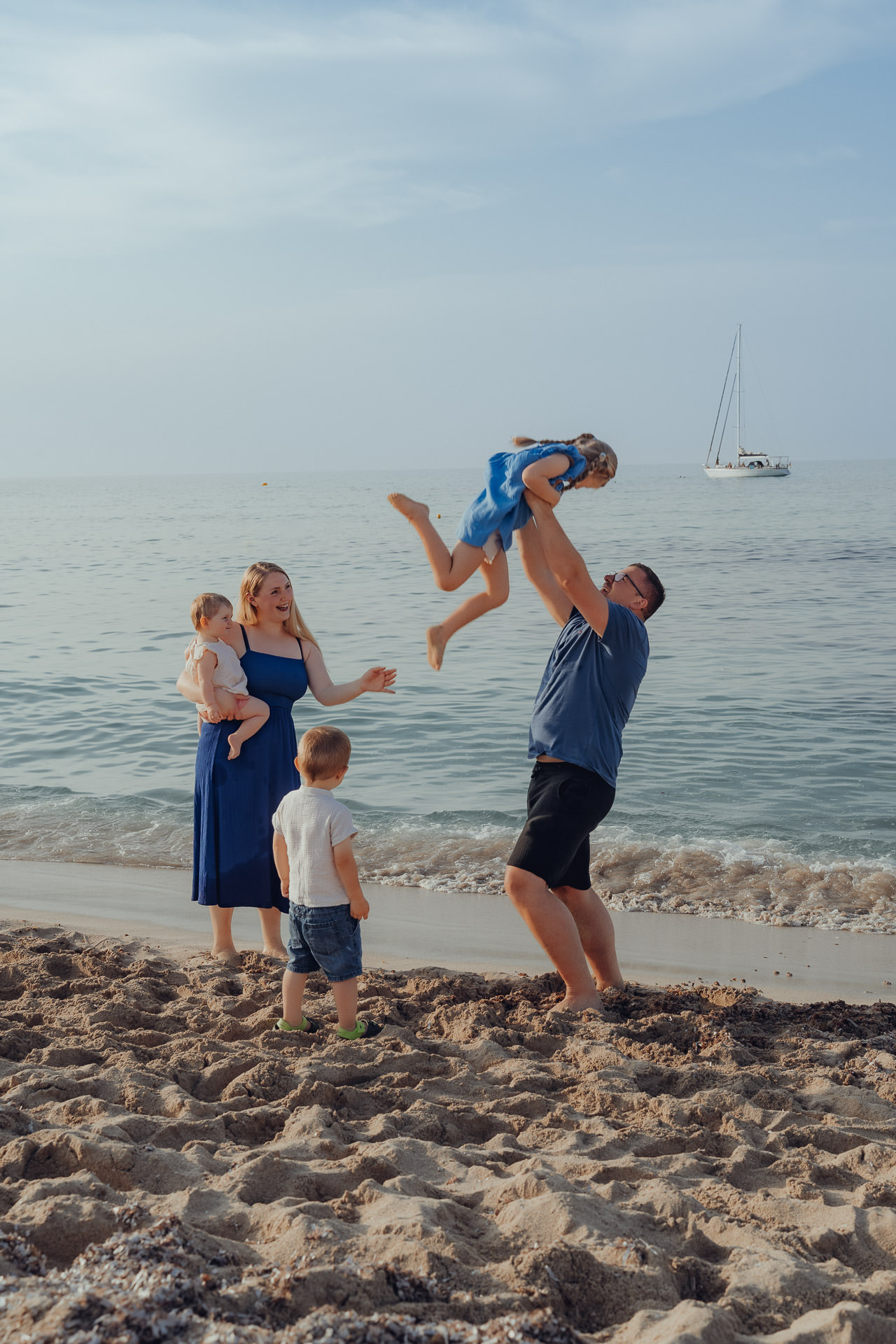 Vater wirft lachende Tochter in die Luft während Familienfotoshooting am Meer in Cala Millor Mallorca