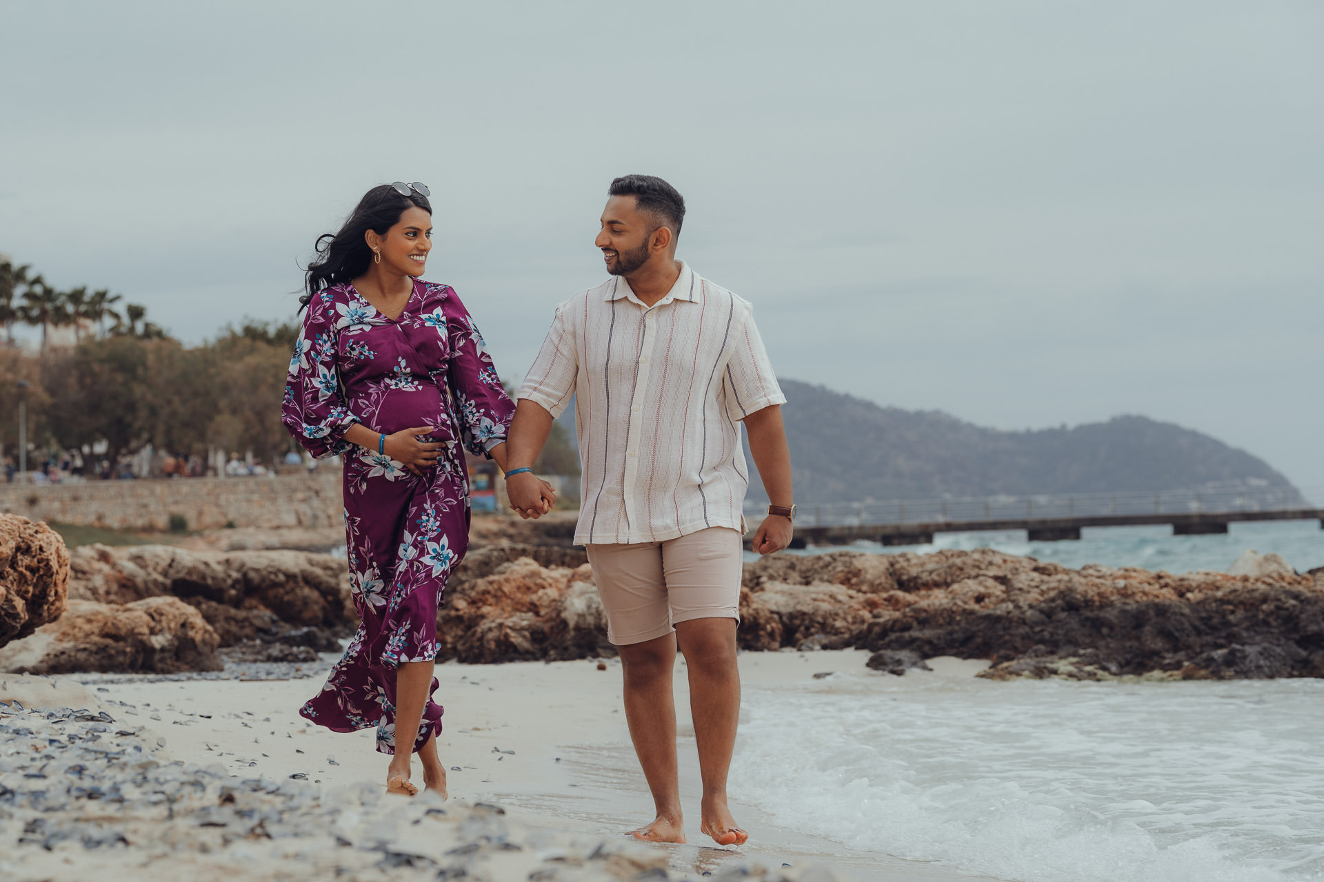 Cala Millor Fotoshooting Junges Paar laufen am Strand von Cala Millor während sie ihren Babybauch hält und beide sich anlächeln
