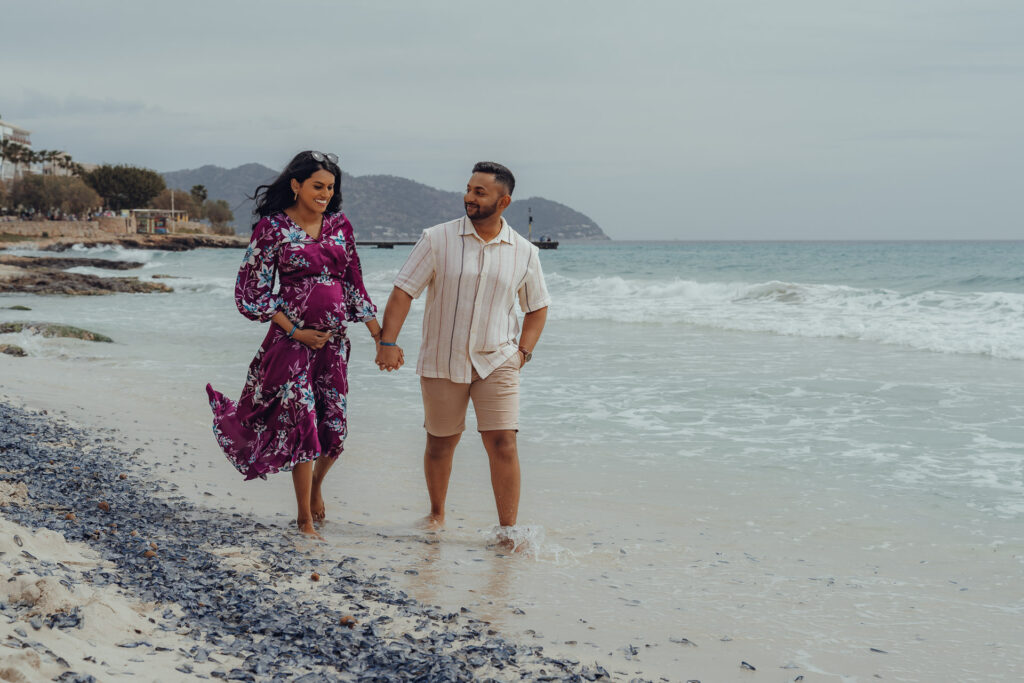 Junges Paar laufen am Strand von Cala Millor während sie ihren Babybauch hält