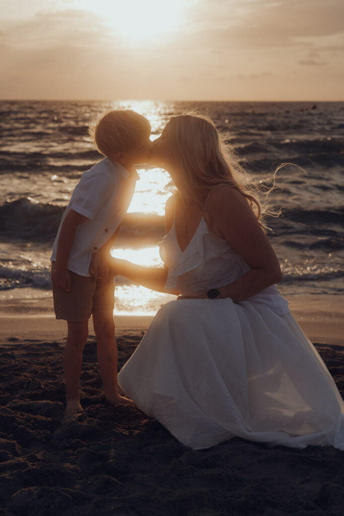 Mutter küsst ihr kleines Kind beim Sonnenaufgang am Strand von Cala Millor