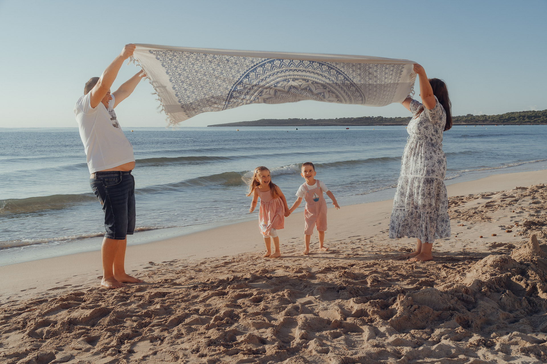 Cala Millor Fotoshooting Mama und Papa halten ein großes Strandtuch hoch, wo die beiden Kinder glücklich drunter her rennen.