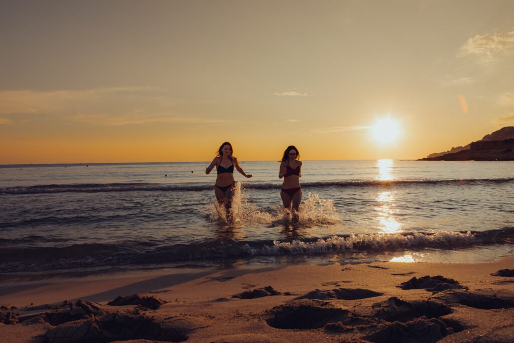 Beste Freundinnen laufen aus dem Meer beim Sonnenaufgang