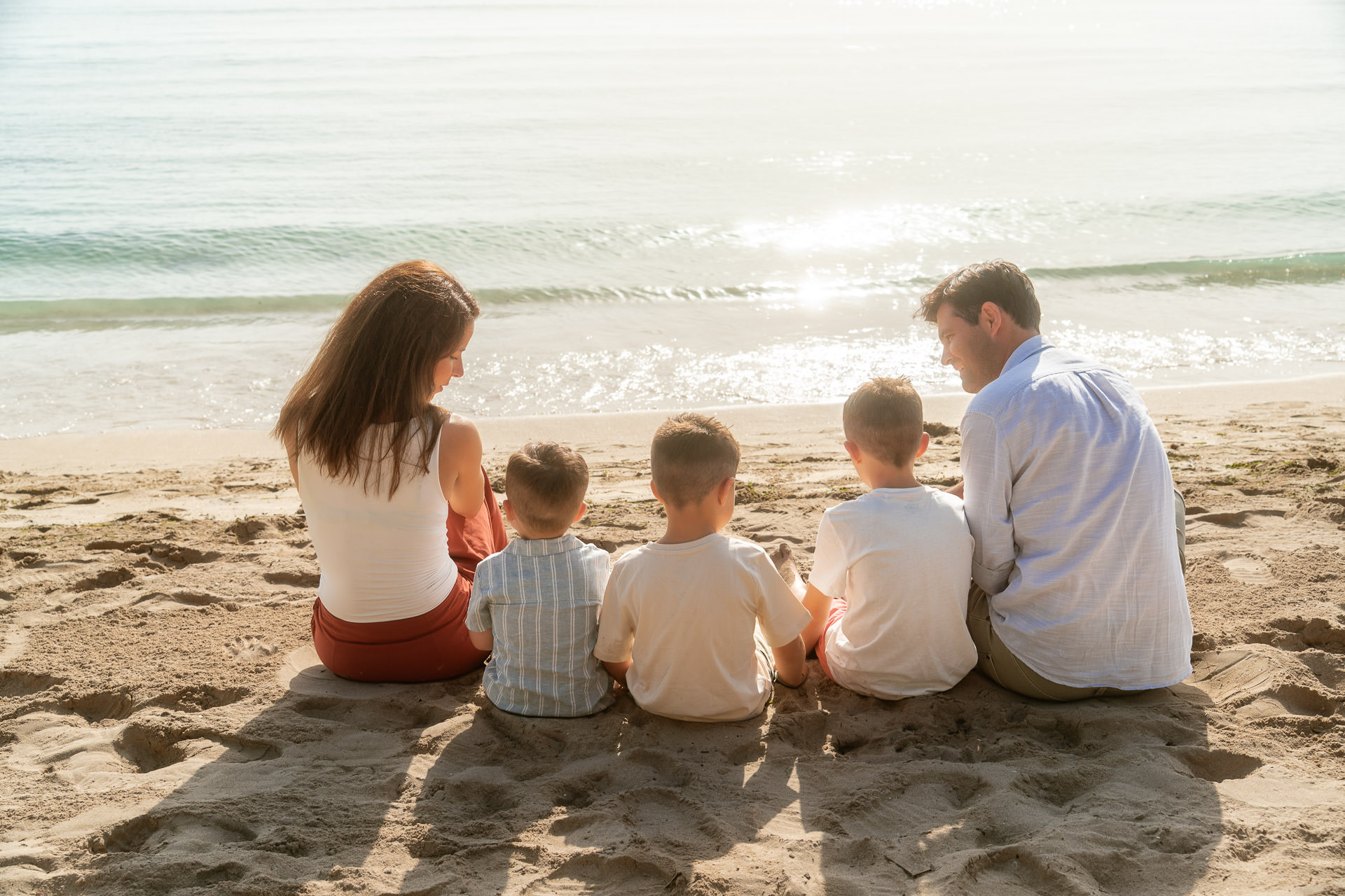 Familie mit drei Kindern sitzt am Strand von Cala Rajada