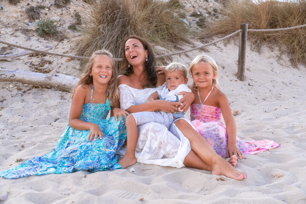Mutter sitzt fröhlich mit ihren drei Kindern im Sand