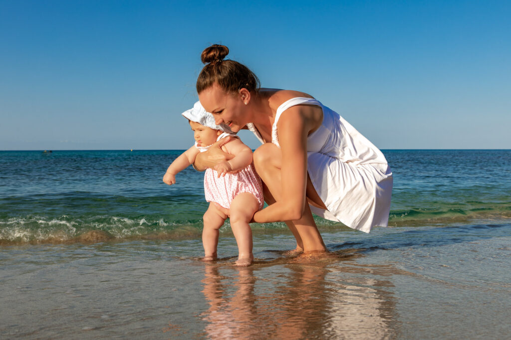 Mutter mit Baby auf dem Armstehen im Meer am Strand von Can Picafort
