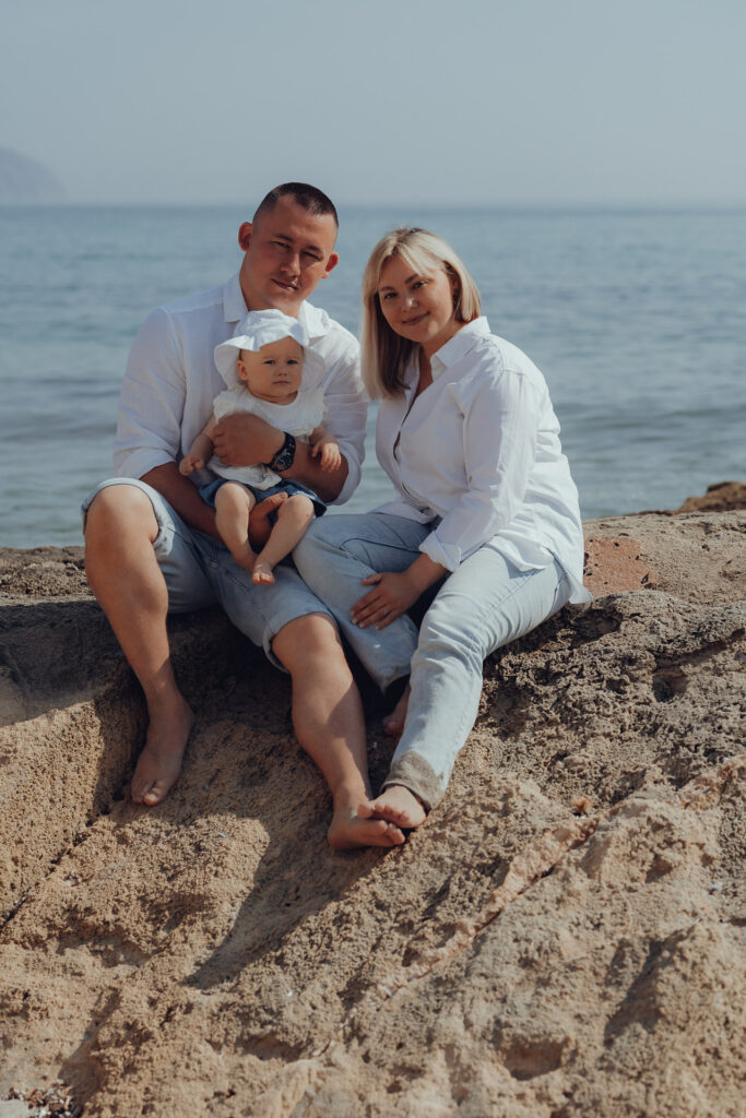 Junge Familie sitzen auf den Felsen am Strand von Can Picafort