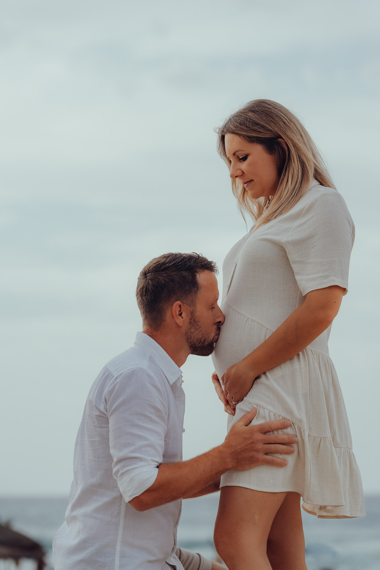 Zärtlicher Moment beim Mallorca Babybauch Shooting – werdender Vater küsst den Babybauch am Meer.