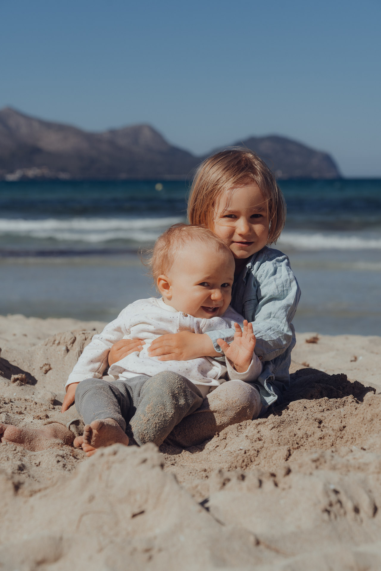 Geschwister sitzen zusammen im Sand am Strand beim Mallorca Familien Shooting