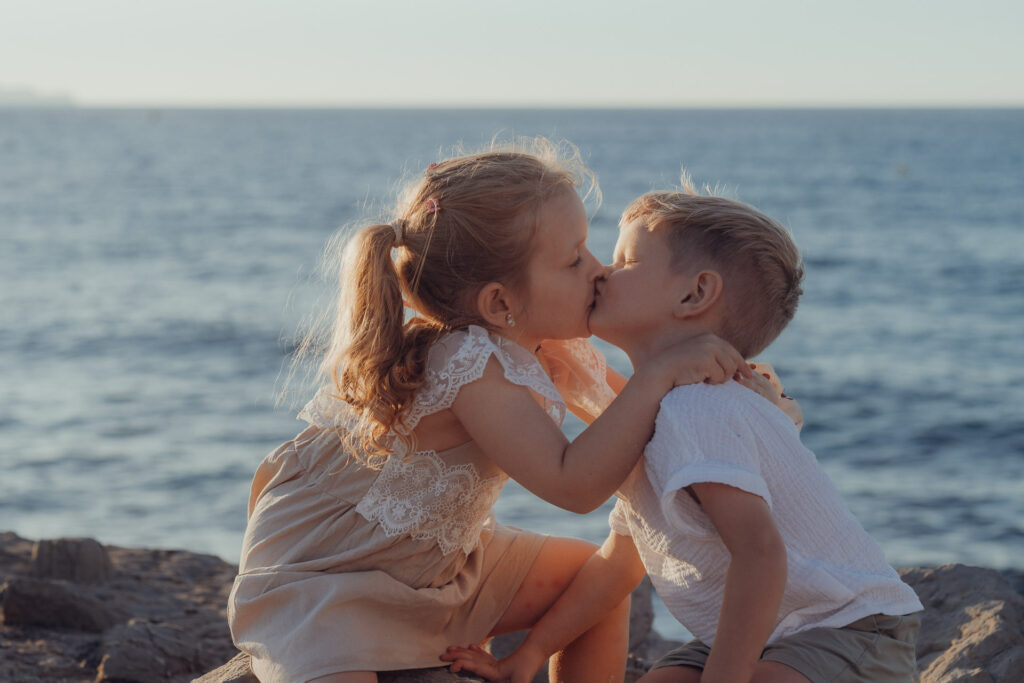 Kleine Geschwister küssen sich im Sand sitzend für ein Fotoshooting