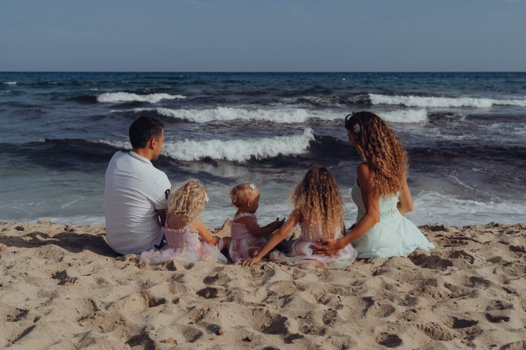 Familie mit drei kleinen Mädchen sitzen am Strand der Cala Mesquida und schauen aufs Meer
