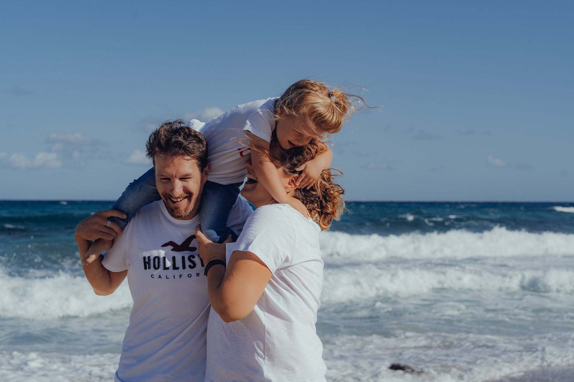 Kind sitzt auf Schultern der Eltern am Meer beim Mallorca Familien Shooting