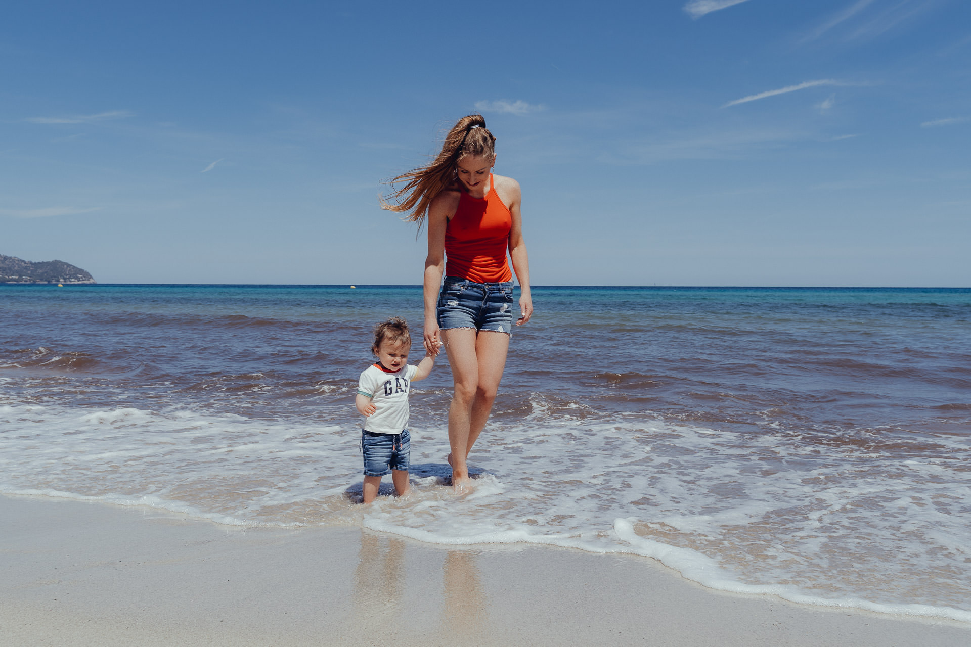 Mutter und Kind gehen Hand in Hand am Meer auf Mallorca