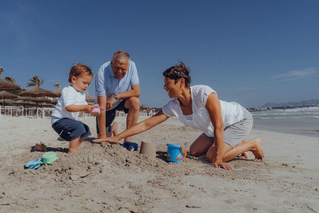 Eltern spielen mit Kind im Sand am Strand von Playa de Muro