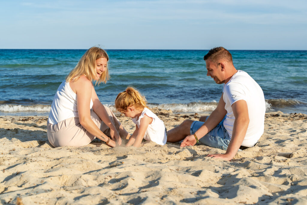 Familie sitzt am Strand und spielt mit dem Kind für ein Fotoshooting