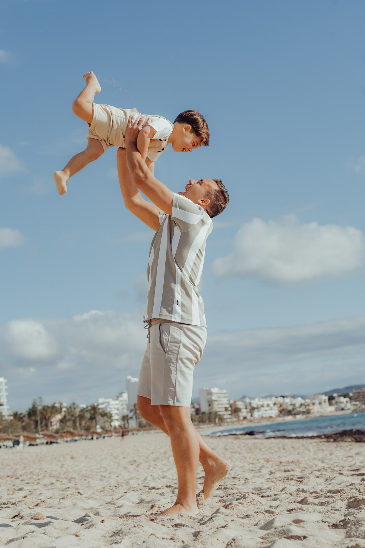 Mallorca Urlaubs Shooting Vater hebt lachendes Kind in die Luft bei einem Strandshooting auf Mallorca – festgehalten vom professionellen Mallorca Fotograf für emotionale Familienmomente.