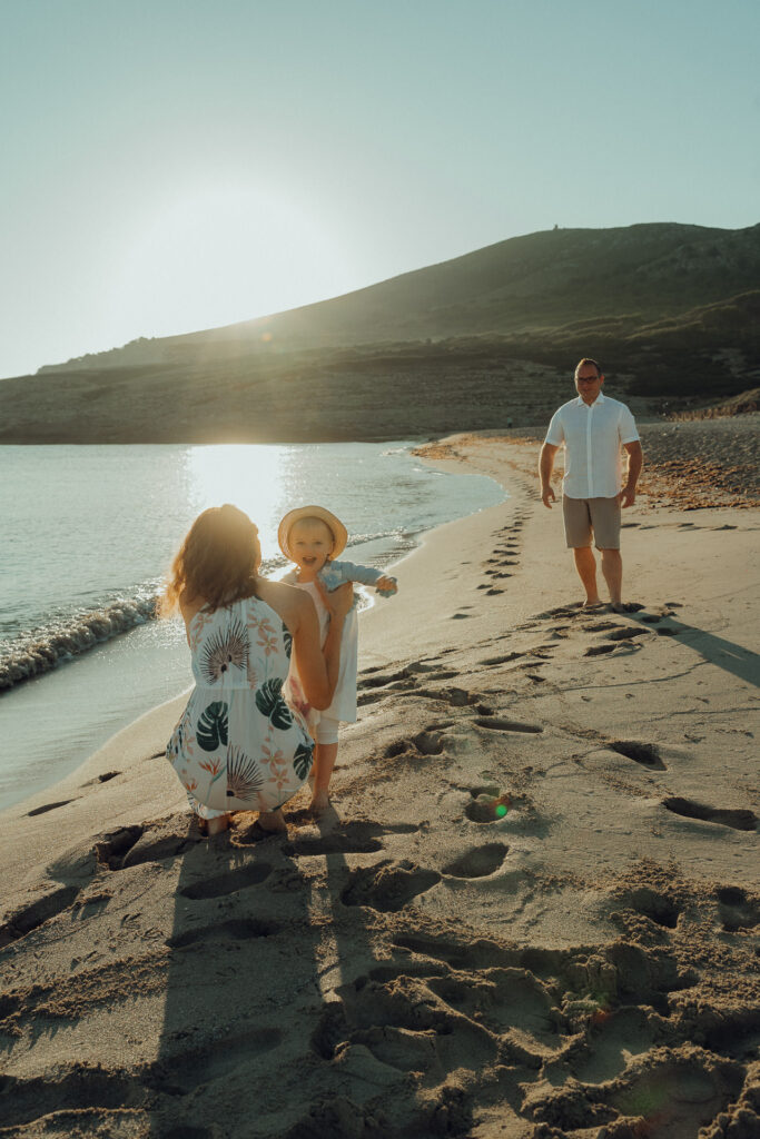 Kleines Kind läuft lachend am Strand vom Papa zur Mama in die Arme