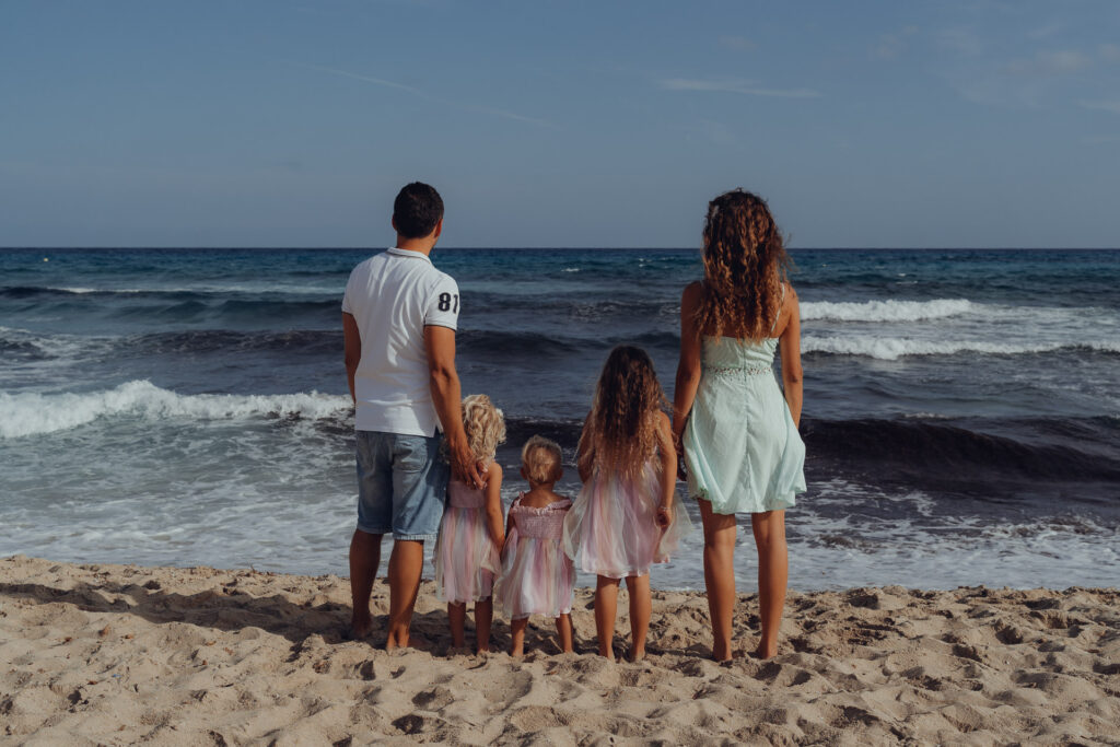 Familie mit drei Kindern stehen am Strand der Cala Mesquida und schauen aufs Meer