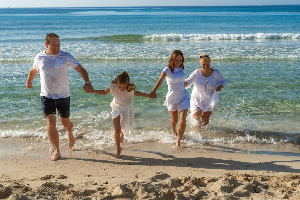 Fröhliche Familie rennt lachend aus dem Meer am Strand von Cala Millor