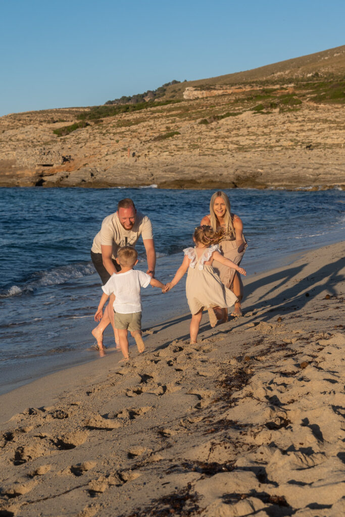Eltern spielen lachend mit zwei kleinen Kindern am Strand von Mallorca in den Abendstunden