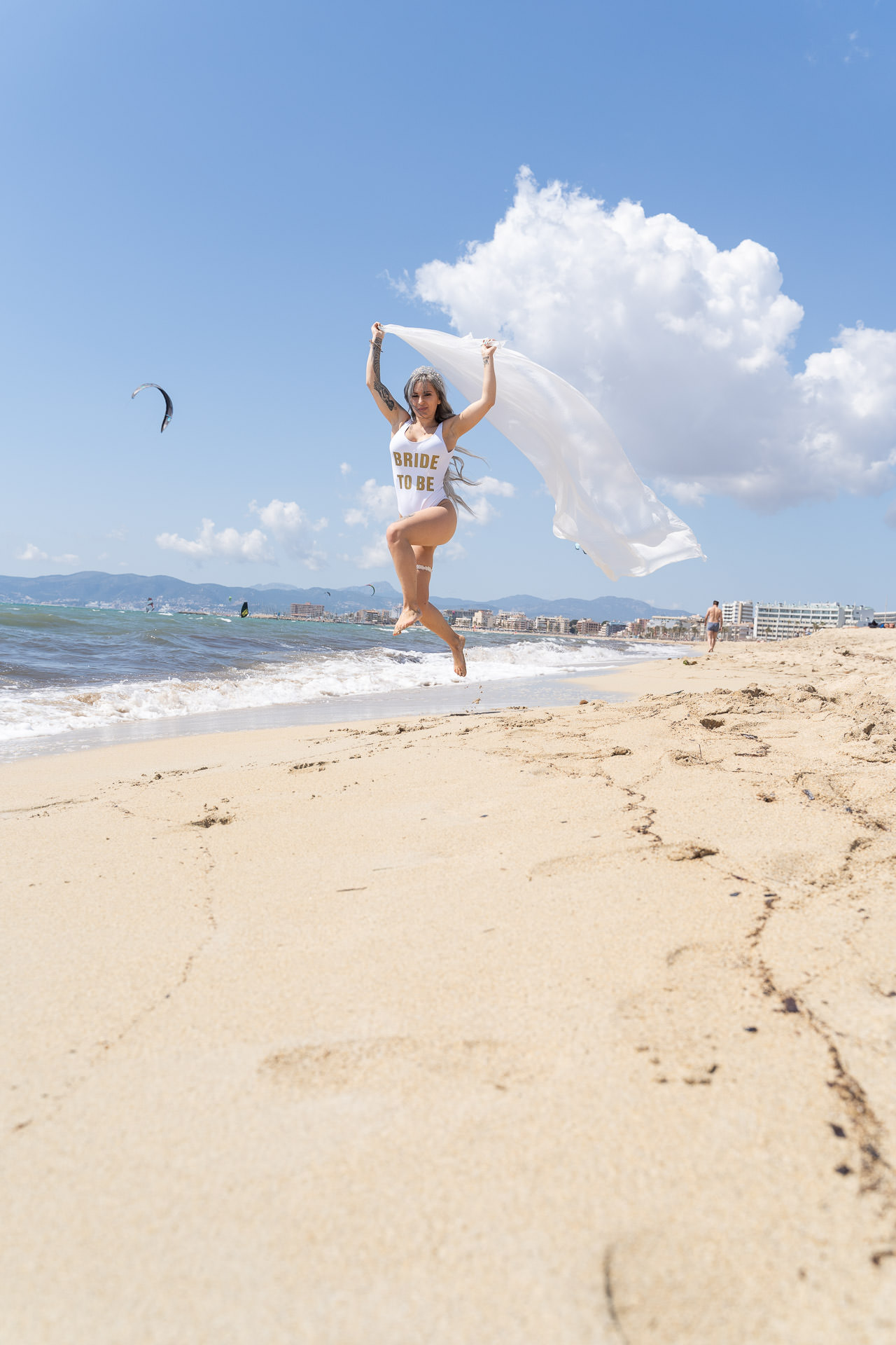 Mallorca JGA Shooting: Braut springt am Strand mit Schleier, blauem Himmel und Meer im Hintergrund.