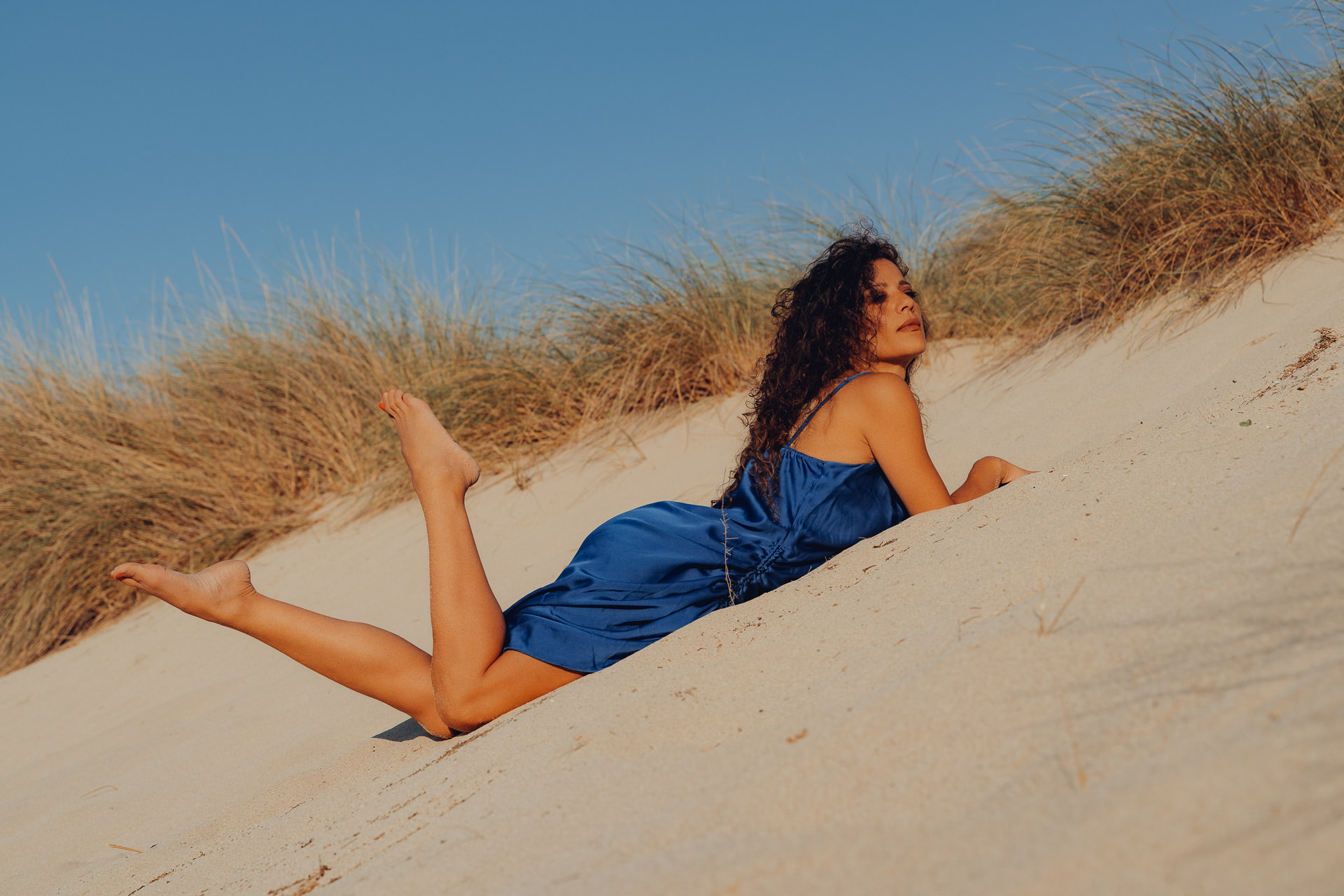 Frau im blauen Kleid liegt auf sonniger Düne mit Blick in die Ferne, Mallorca Model Shooting