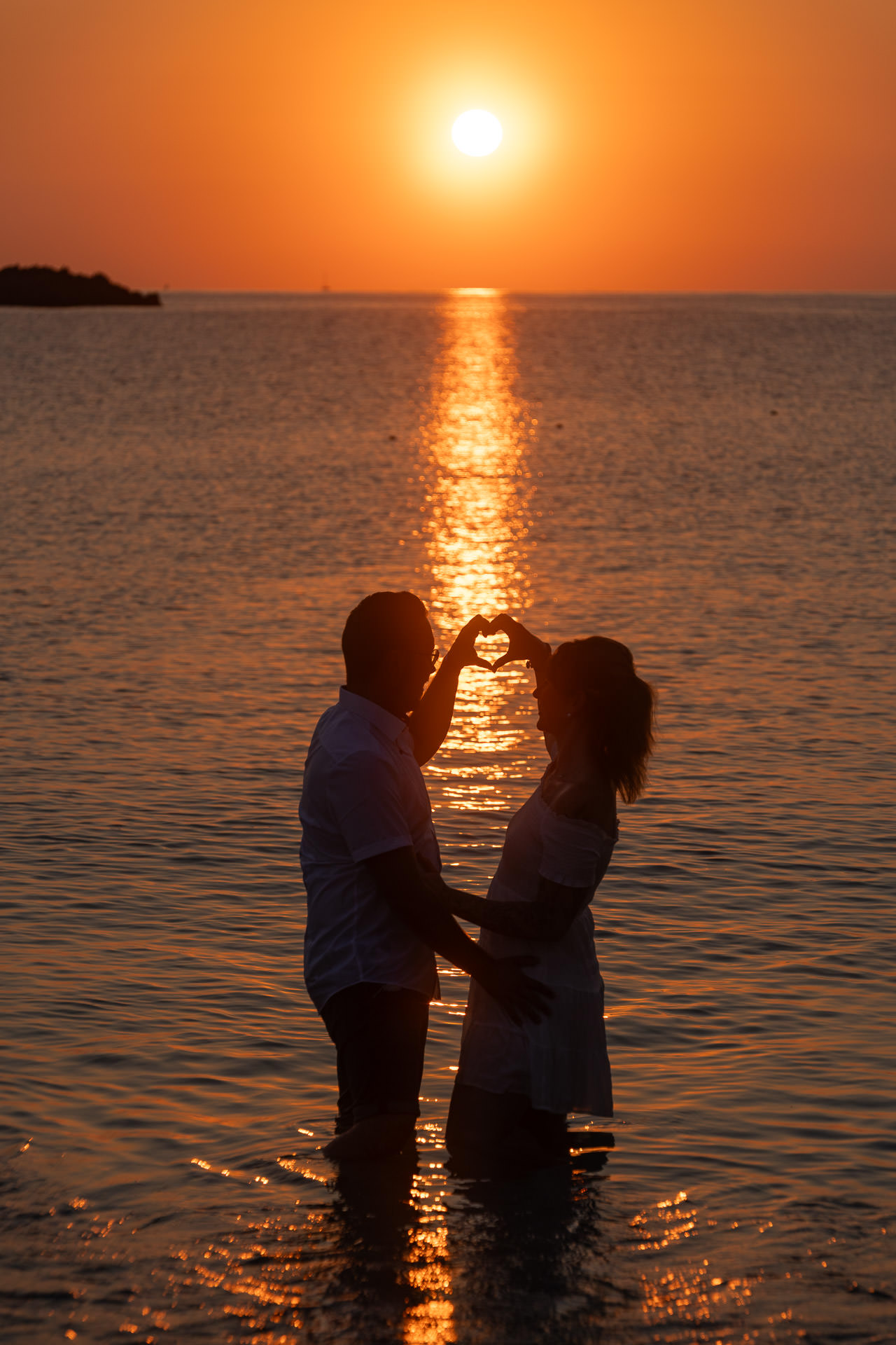 Mallorca Sonnenaufgang Shooting Junges Paar hält mit den Händen ein Herz in die Luft, im Hintergrund geht die Sonne auf Mallorca auf.