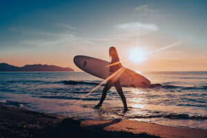 Model mit Surfbrett läuft bei Sonnenaufgang am Strand in Cala Millor