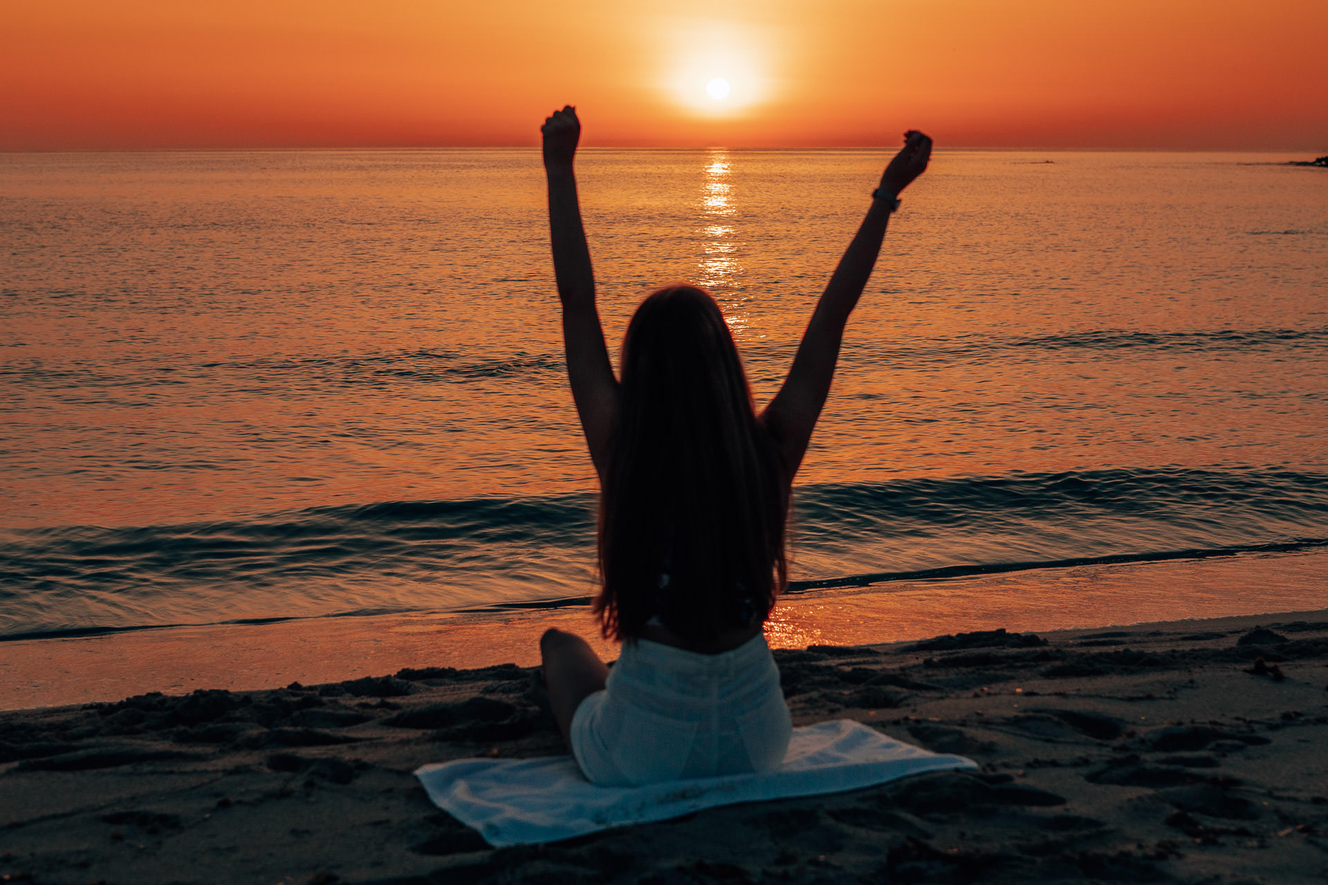 Mallorca Sonnenaufgang Shooting Model sitzt am Strand von Cala Millor und schaut zum Sonnenaufgang, dabei hält sie die Arme hoch