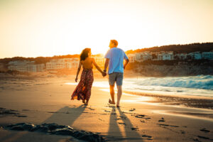 Paar läuft Hand in Hand an der Cala Mesquida und im Hintergrund geht die Sonne unter