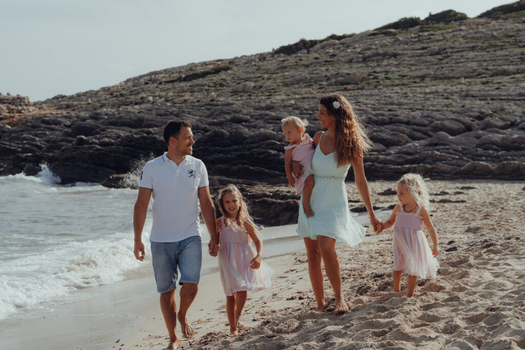 Eine glückliche Familie mit drei kleinen Mädchen läuft am Strand von Mallorca