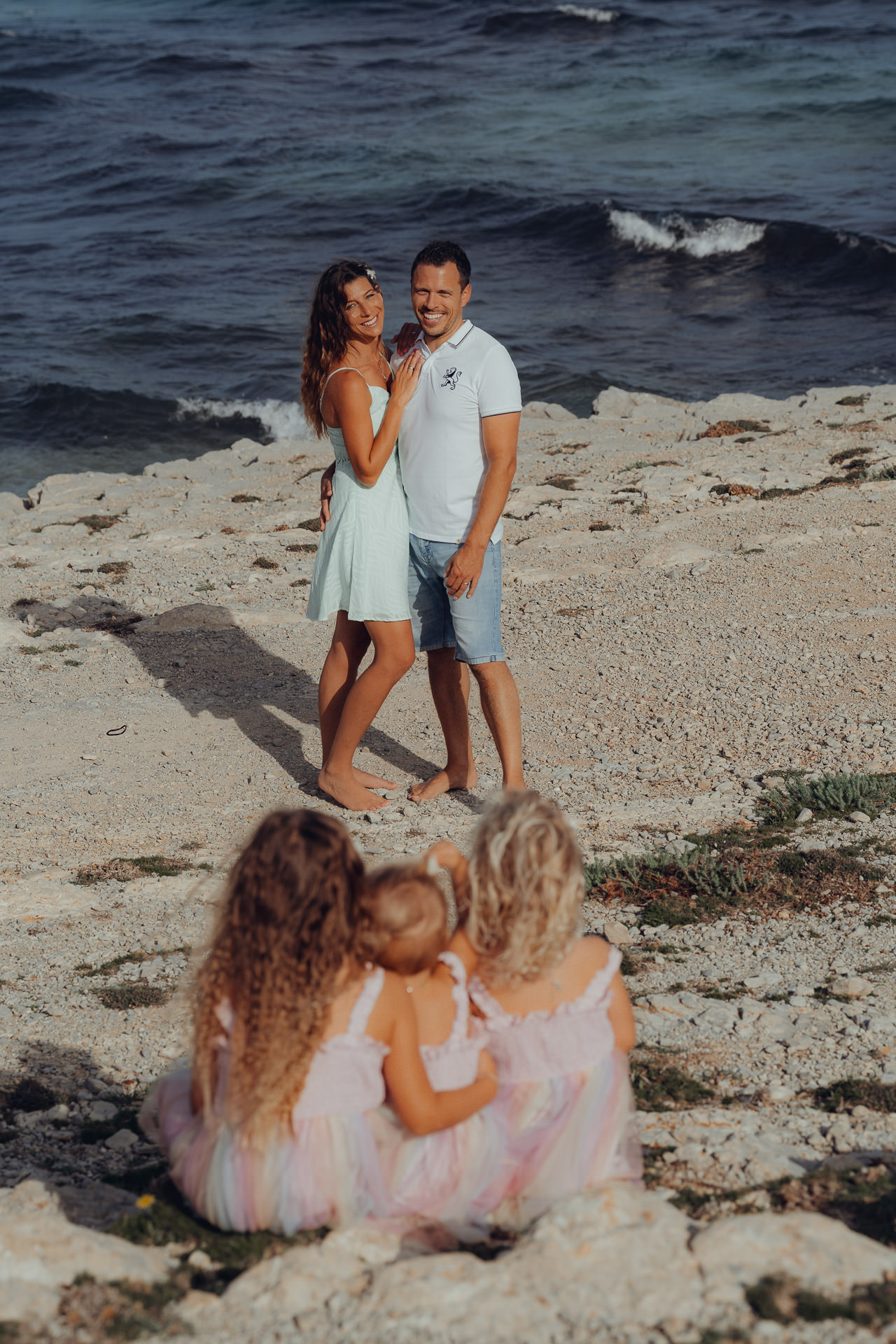 Mallorca Urlaubs Shooting Drei kleine Mädchen schauen sitzend zu den glücklichen Eltern
