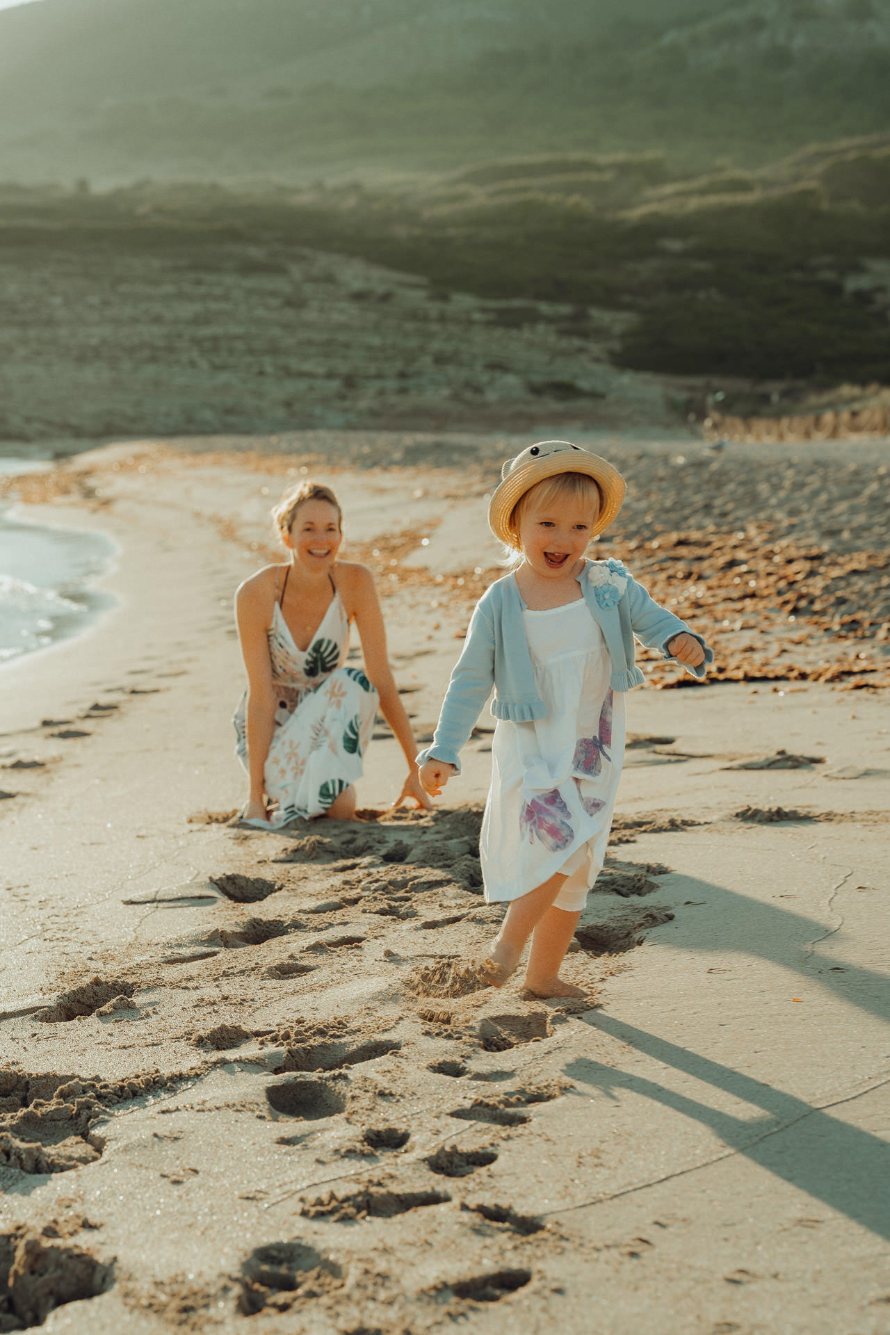 Mallorca Urlaubs Shooting Ein kleines Mädchen läuft lachend bei Sonnenuntergang am Strand von der Mutter weg.