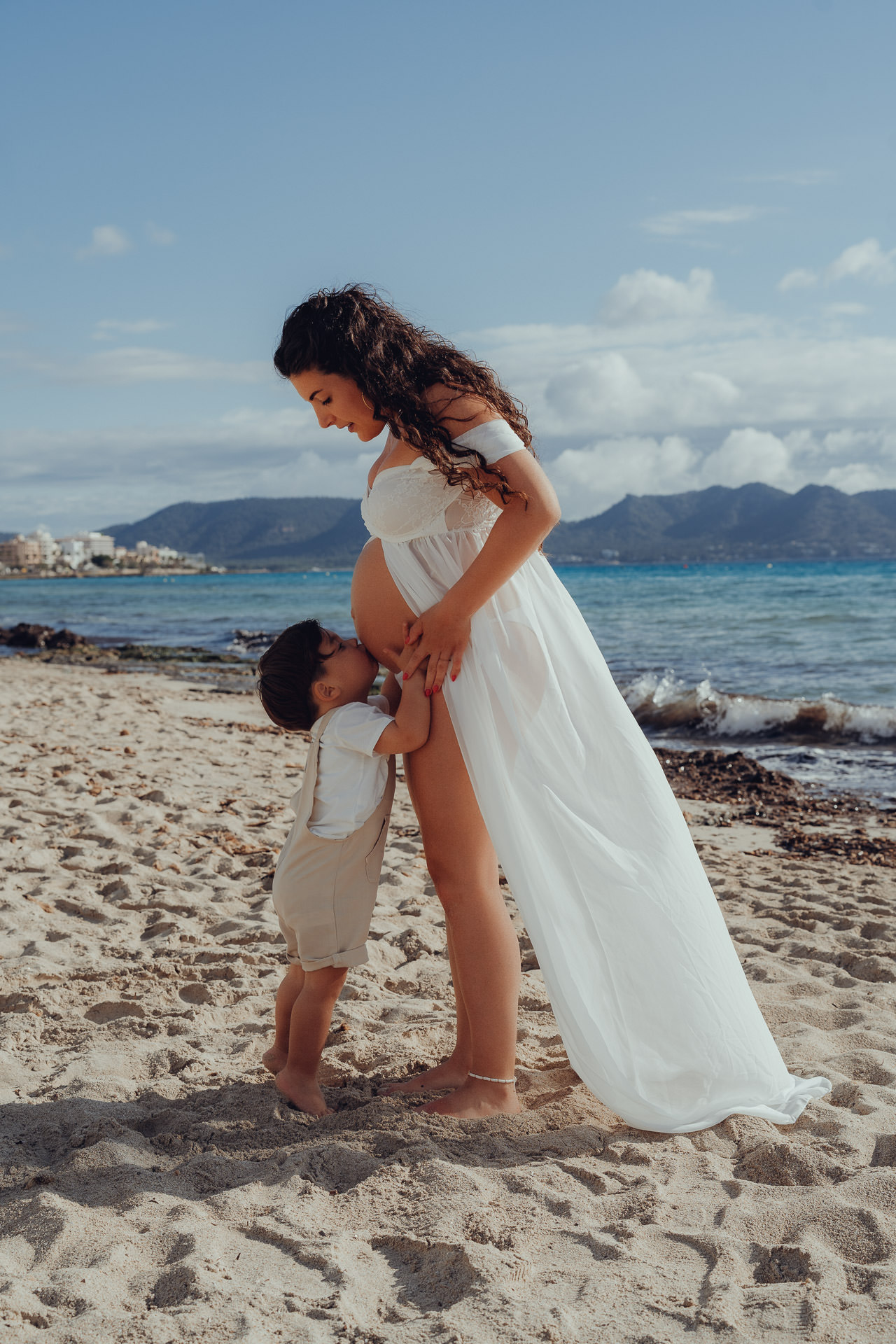Playa de Muro Fotoshooting Kind küsst den Babybauch der Mutter am Strand