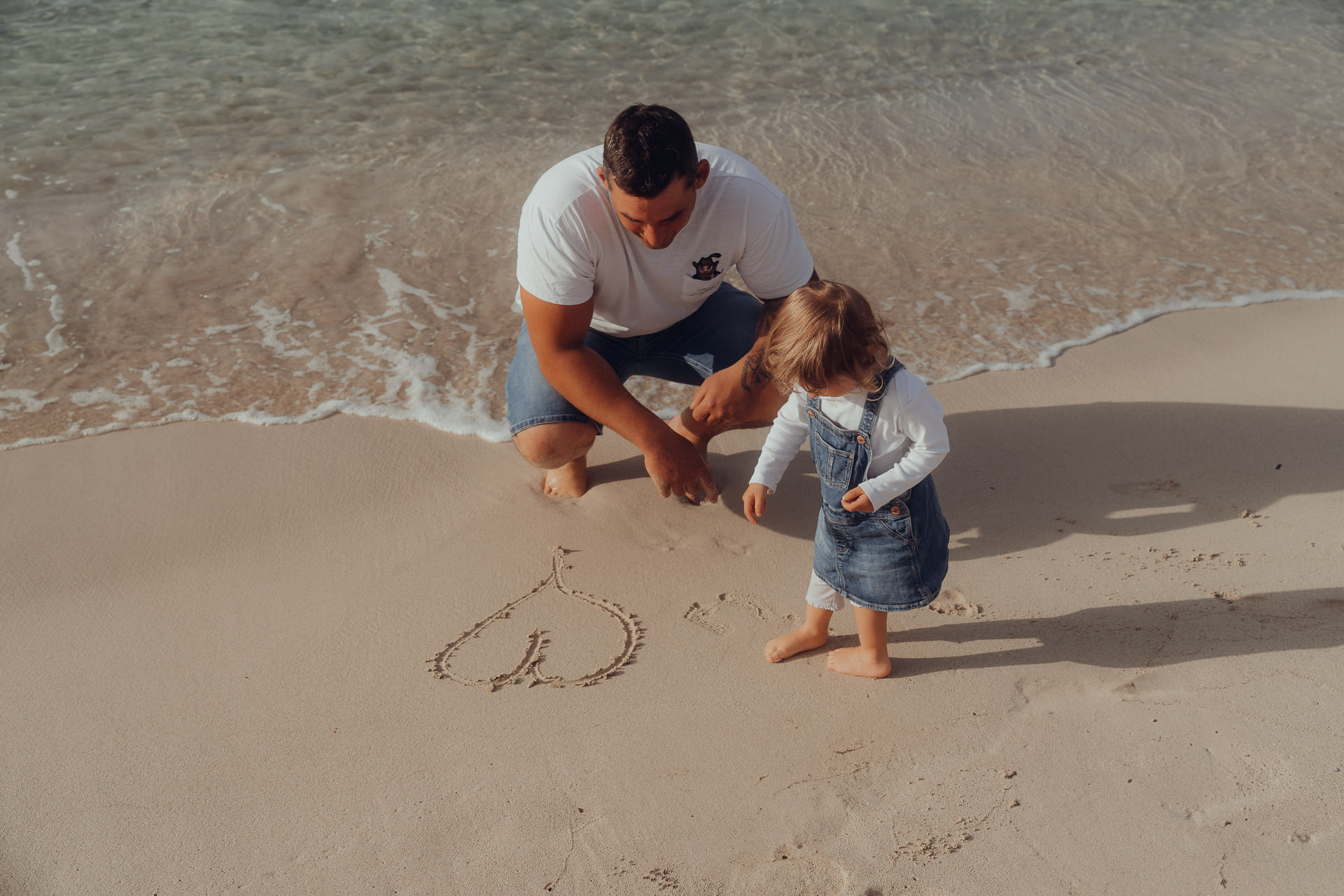 Playa de Muro Fotoshooting Papa malt mit kleiner Tochter ein Herz in den Sand der Playa de Muro