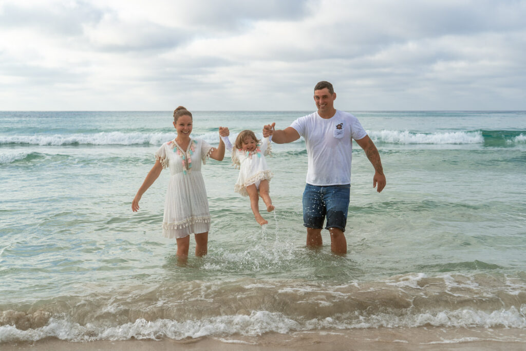 Familie steht im Meer von Sa Coma und hält das kleine Mädchen hoch