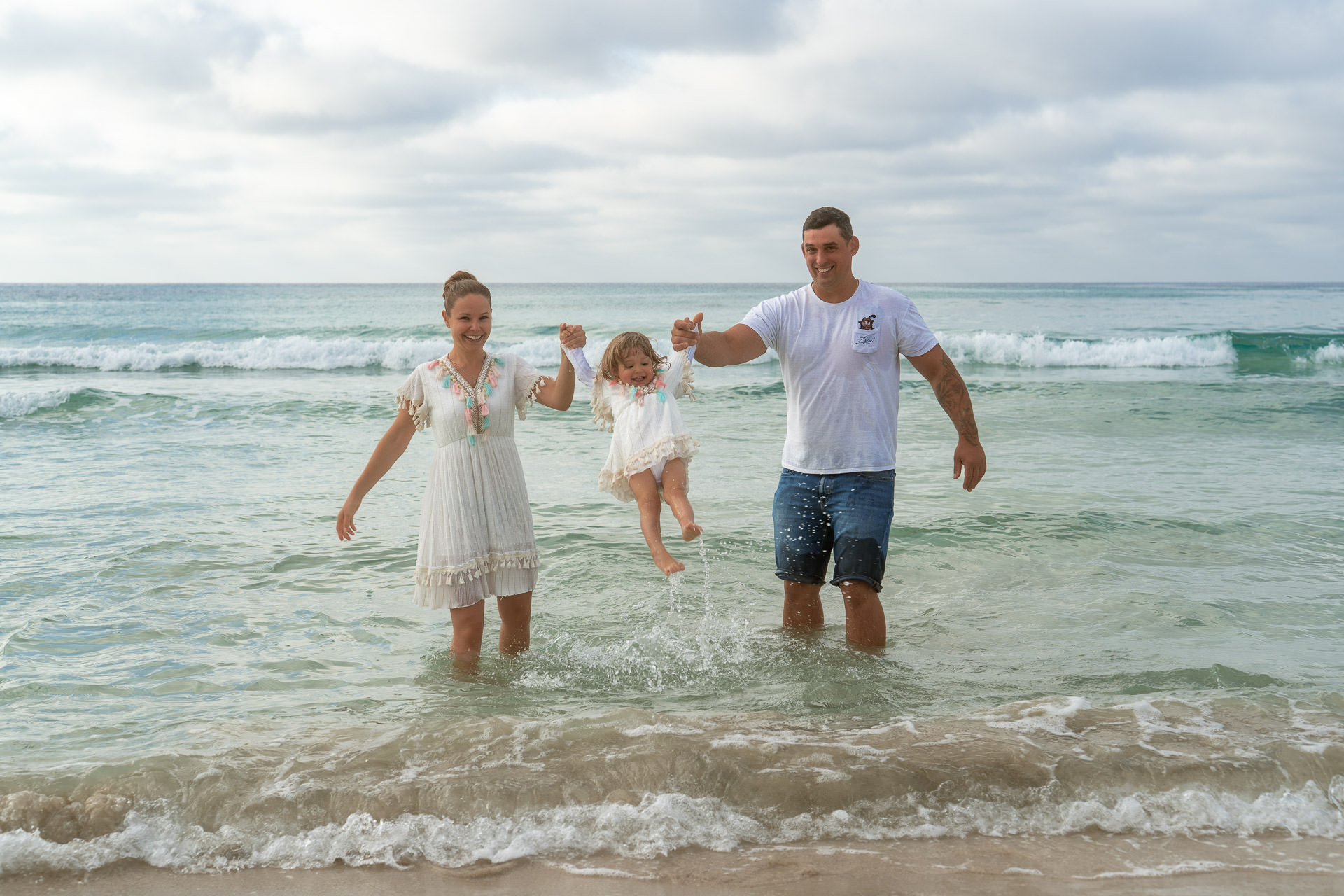Sa Coma Fotoshooting Familie steht im Meer von Sa Coma und hält das kleine Mädchen hoch