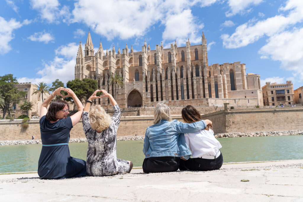 Vier Frauen sitzen am Wasser vor der Kathedrale La Seu in Palma und feiern gemeinsam den Moment.