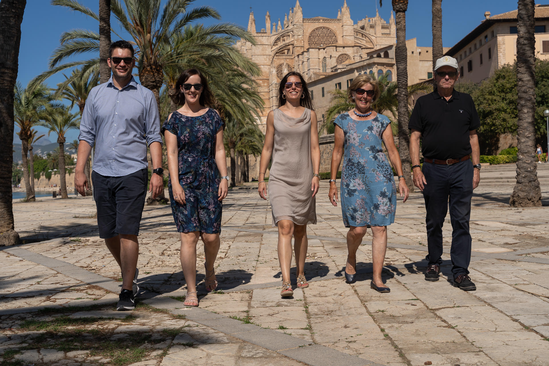 Gruppe läuft unter Palmen Richtung Kathedrale La Seu in Palma, Sommertag auf Mallorca.