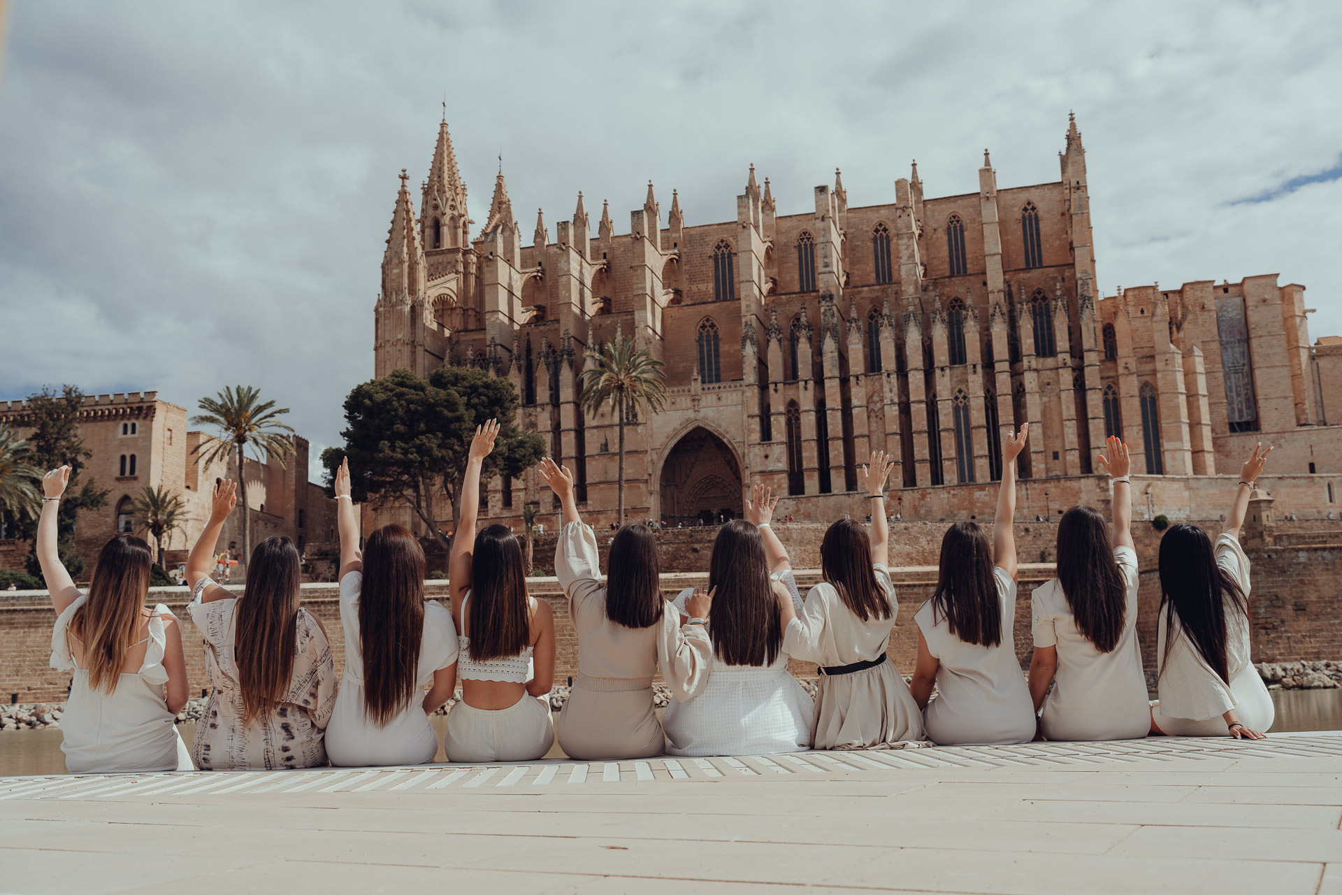Junge Frauen sitzen mit erhobenen Armen am Ufer vor der Kathedrale von Palma.
