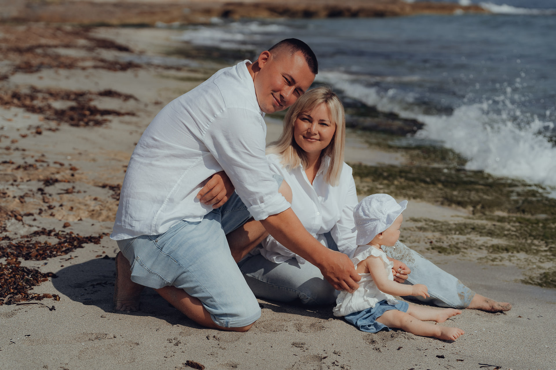 Familienfoto beim Sa Coma Fotoshooting: Eltern sitzen mit ihrem Baby entspannt am Strand von Sa Coma.