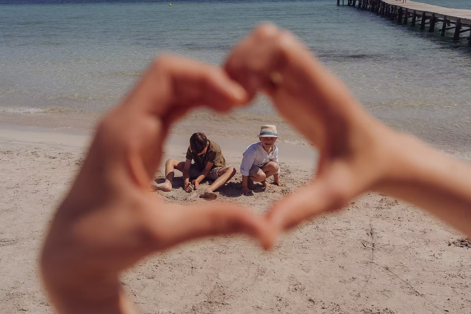 2 Kinder spielen im Sand am Meer und sind im Handherz zu sehen.