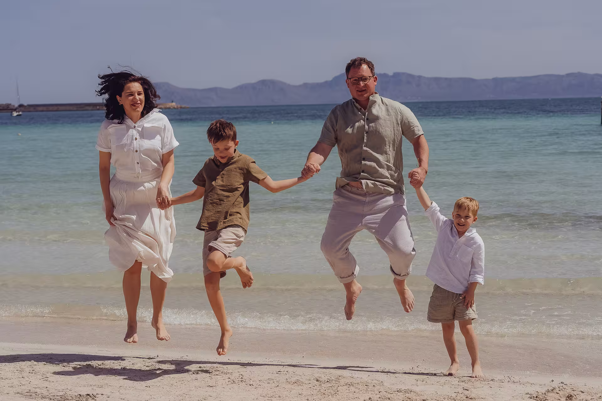 Familie mit 2 Kindern springt gemeinsam am Strand hoch.