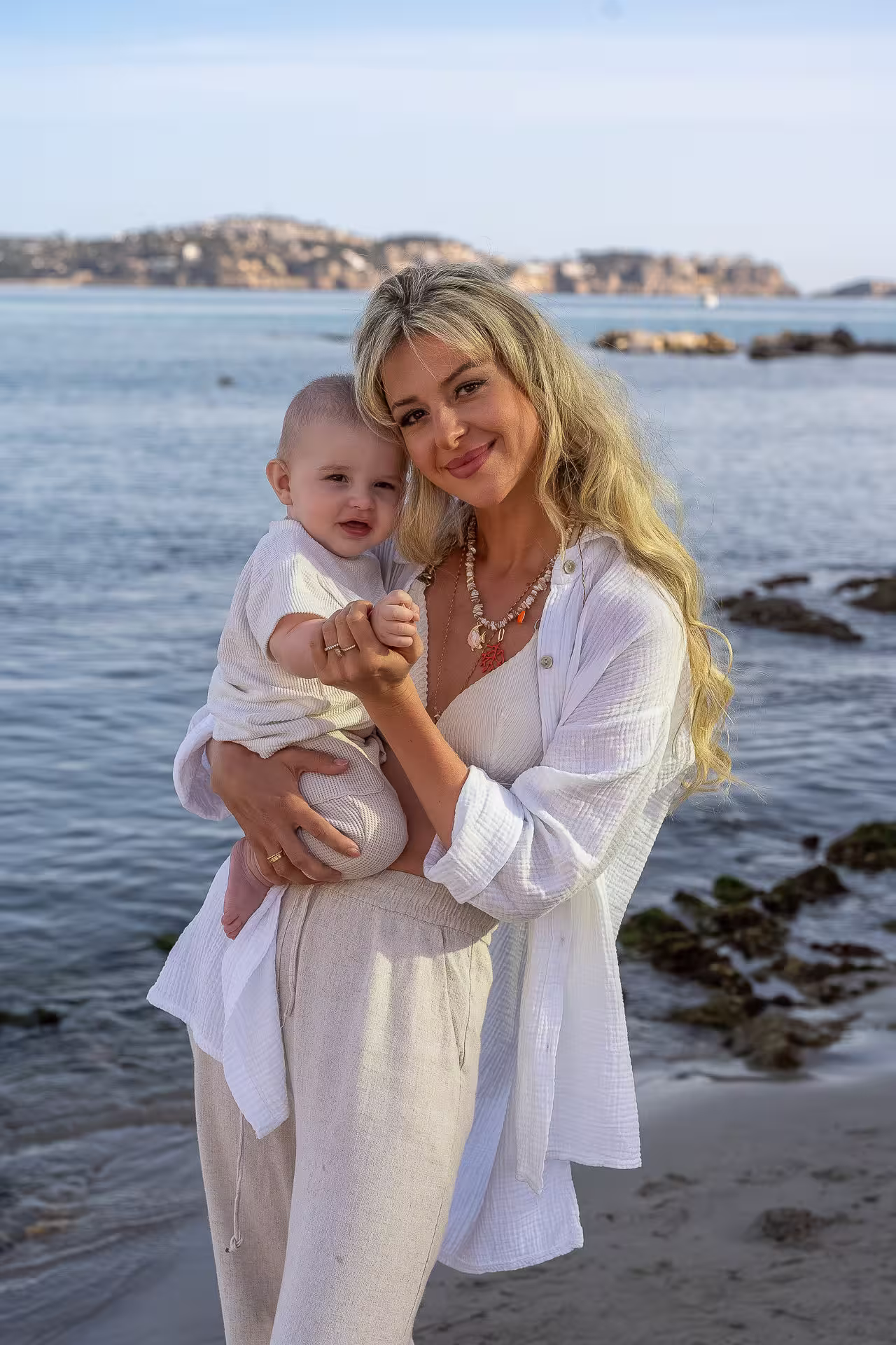 Junge Mutter mit Baby auf dem Arm steht am Meer
